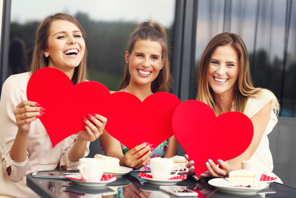 Three smiling women sitting and holding three red paper hearts